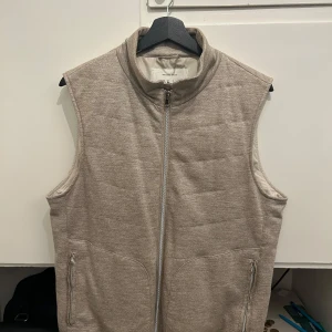 Beige quiltad dunväst från L.B.M. 1911 - Nog den Snyggaste beige dunvästen från L.B.M. 1911 med quiltad design som du kan hitta! Västen har två fickor med dragkedja framtill och två innerfickor med knapp. Materialet är mjukt och har en diskret textur, perfekt för lager-på-lager. Stängs med dragkedja hela vägen upp.