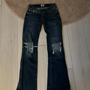 Mörkblå bootcut jeans med hål XS - Snygga mörkblå jeans från 157 i bootcut-modell med slitna, stora hål över knäna. Låg midja och klassisk femficksdesign. Jeansen har en cool, avslappnad vibe och är gjorda i ett robust denimtyg.