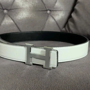 Vitt bälte med H-spänne - Snyggt vitt bälte med ikoniskt H-spänne i silverfärg. Bältet är gjort i skinn och har en stilren, klassisk design som passar till många outfits. Insidan är svart vilket ger en cool kontrast. Perfekt accessoar för att lyfta din look. Den är 110 cm lång