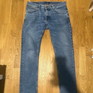 Nudie Jeans Grim trim  - Säljer ett par klassiska blå jeans från Nudie Jeans i modellen Grim trim. Tillverkade i mjuk bomullsdenim med en lätt tvättad look. Perfekta för dig som gillar stilrena och tidlösa jeans. Jeansen har krympt lite så passar även mindre storlekar.