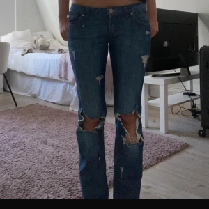 Blå slitna bootcut jeans - Säljer ett par blå jeans med bootcut passform och slitningar. Jeansen är lågmidjade. Köpta för: 480kr