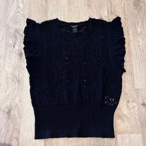 Svart stickad topp med volang från Lindex S - Svart stickad topp från Lindex med volangärmar och ett fint hålmönster. Strl S