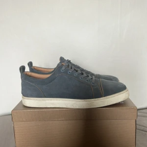 Blå mockasneakers från Louboutin - Snygga blå sneakers i mocka från Louboutin med klassiska röda sulor. Skorna har rund tå, snörning och en vit platt sula. Insidan är beige och detaljerna är diskreta men lyxiga. Perfekta för dig som gillar stilrena och exklusiva sneakers. Bra skick 8/10 inte använda så mycket. Hör gärna av er om ni har frågor 