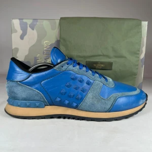 Valentino Rockrunnerr - Snygga Valentino Rockrunner sneakers i blått skinn och mocka med coola pyramidnitar på sidorna. Skorna har blå snörning, rund tå och beige mellansula. Perfekt för dig som vill sticka ut med ett lyxigt streetwear vibe. Kommer med originalkartong och dustbag.