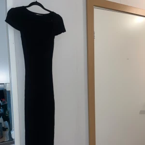 Svart ribbad långklänning Gina Tricot - Säljer en svart ribbad långklänning från Gina Tricot. Klänningen har korta ärmar, figurnära passform och en snygg v-ringning. Materialet är stretchigt och mjukt, perfekt för dig som gillar en stilren look med lite edge.