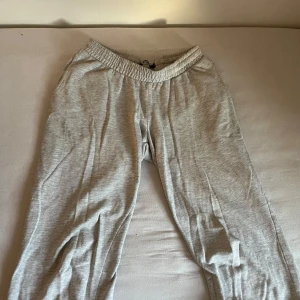 Grå mjukisbyxor med resårmidja - Säljer ett par ljusgrå mjukisbyxor med elastisk midja och raka ben. Perfekta för chill dagar eller när du vill vara extra bekväm. Byxorna är gjorda i mjukt bomullsmaterial och har en enkel, stilren look utan synliga loggor eller detaljer. Dessa har krympt lite i tvätten också!! 