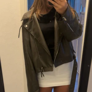 Svart skinnjacka med dragkedjor - Säljer en svart skinnjacka med coola dragkedjor och breda slag. Jackan har en oversized passform och långa ärmar, perfekt för att lyfta vilken outfit som helst. Snygga detaljer som snörning och bälte ger en edgy vibe.