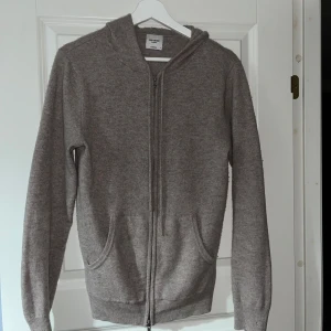 Beige cashmere hoodie från John Henric - Säljer en lyxig beige hoodie från John Henric i mjuk cashmere. Tröjan har dragkedja framtill och praktiska fickor. Perfekt för kyliga dagar med sin sköna huva och långa ärmar. Passar både till vardags och mer avslappnade tillfällen. 100% Kashmir