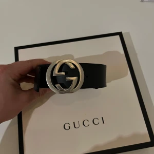 Svart skärp med silverfärgat spänne från Gucci - Snyggt svart skärp från Gucci i skinn med ett ikoniskt silverfärgat G-spänne. Perfekt för att ge en lyxig touch till din outfit. Tillverkat i Italien med handmålade kanter och palladiumtonad hårdvara.