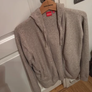 Beige stickad tröja - Säljer en mysig beige hoodie från Vero Moda. Den har en dragkedja framtill och en praktisk huva med snörning. Perfekt för en avslappnad stil.