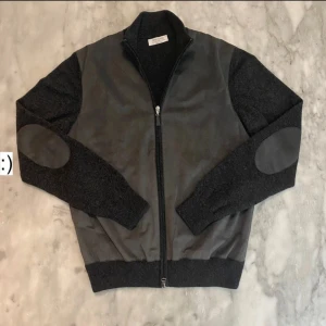Grå jacka från Gran Sasso - Gran Sasso cardigan i väldigt bra skick.Enda defekten är taggen i nacken som släppt på en sida men är inget som förändrar skicket av plagget. I ull och Kashmir blandning med mocka på framsidan samt armbågarna. I färgen svart och grå med storlek 48 vilket är som M men väldigt liten i storlek så passar S   Mått: Bröst bredd:50cm Längd:63cm Inre ärmlängd:47 cm Yttre ärmlängd:62 cm | Nypris 4299kr