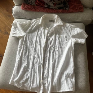 Vit kortärmad linne skjorta från DeFacto - Säljer en vit kortärmad linne skjorta från DeFacto i regular fit. Skjortan har en klassisk krage och knappar framtill samt en bröstficka. Perfekt för en avslappnad stil.