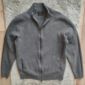 Grå tröja från Massimo Dutti - Säljer en stilren grå kofta från Massimo Dutti i bomull. Koftan har en dragkedja framtill och en hög krage. Perfekt för kyligare dagar och passar till många olika stilar. Ett måste i garderoben för den som gillar klassisk design. Storlek M men sitter mer som S