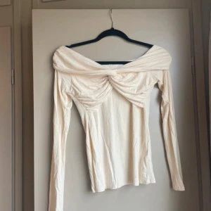 Beige offshoulder topp - Säljer en elegant beige offshoulder topp med långa ärmar och en knutdetalj framtill. Perfekt för flera olika tillfällen!