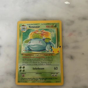 Venusaur Pokémonkort - Säljer ett holografiskt Venusaur Pokémonkort med 100 HP. Kortet har en grön ram och visar Venusaur med en stor blomma på ryggen. Det har attacken Solarbeam med 60 skada och en speciell förmåga kallad Energy Trans. Perfekt för samlare eller Pokémon-entusiaster!