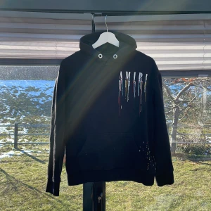 Amiri hoodie - Säljer en svart hoodie från Amiri med färgade snygga detaljer på både framsidan och baksidan. Storlek: Small, skulle rekommendera den för någon mellan 165-175 cm lång då jag knappt får på den och är 180 cm, kom dm vid frågor bud eller funderingar.