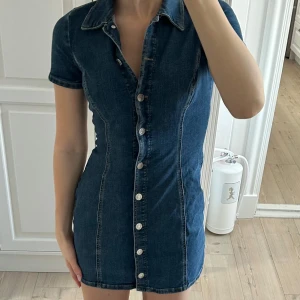 Jeansklänning från Monki - Snygg jeansklänning från Monki i mörkblå denim. Klänningen har korta ärmar och knappar längs hela framsidan💕