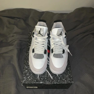 Jordan 4 miltary black - Snygga vita och svarta Nike Air Jordans med klassisk design. Skorna har snörning och en ikonisk logga på hälen. Perfekta för dig som vill ha stil och komfort i ett.