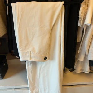 Vita byxor från Bershka - Snygga vita byxor från Bershka med knappdetalj vid midjan.Tillverkade i ett lätt och bekvämt material.