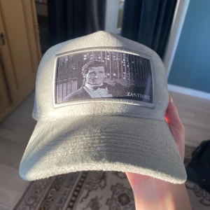 Grå keps från Zantiore - Snygg grå keps från Zantiore med ett tryck framtill. Kepsen har ett nätmaterial på sidorna och baksidan för extra ventilation. Perfekt för en avslappnad stil.  Tyckte inte den passade min stil så använd ca 3 gånger. Priset kan diskuteras. Nytt pris 600 mitt pris 250