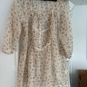Blommig klänning/tunika  från Isolde - Charmig blommig klänning från Isolde i ljusa toner med trekvartsärm och knappar framtill. Perfekt för en romantisk look med sin luftiga passform och söta blommönster. Tunn. Storlek XL fint danskt märke 