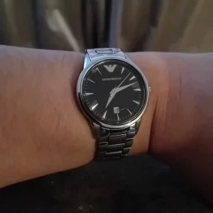 Silverfärgad klocka från Emporio Armani - Stilren klocka från Emporio Armani med svart urtavla och datumvisning. Klockan har en silverfärgad metallarmband och tydliga visare. Perfekt för den som söker en elegant accessoar.