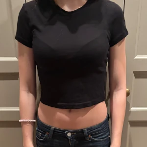 Svart croppad t-shirt - Säljer en stilren svart croppad t-shirt med korta ärmar. Perfekt för en avslappnad look. Passar bra till jeans eller kjol.