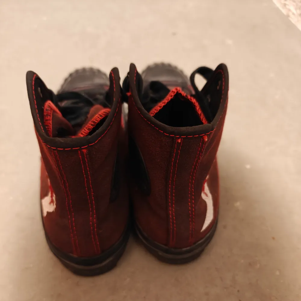 Snygga röda sneakers med svarta sulor och snörning. Skorna har röda sömmar och en unik vit och röd broderad detalj på sidan. Perfekta för en cool och avslappnad stil.. Kengät.