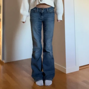 Blå Superlow Boot Jeans från Levi's - Snygga blå jeans från Levi's i modellen Superlow Boot. De har en låg midja och bootcut-stil som ger en avslappnad look. Perfekta för en casual outfit. Klassisk femficksdesign med Levi's ikoniska läderlapp bak.