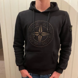 Svart hoodie från Stone Island - Säljer en svart hoodie från Stone Island med det ikoniska kompassmärket på bröstet och ärmen. Tröjan har en justerbar huva med snören. Tröjan är knappt använd och i väldigt fint skick utan några defekter, 9/10. Skriv vid frågor och funderingar😁
