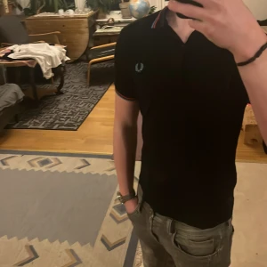 Svart pikétröja från Fred Perry - Säljer en stilren svart pikétröja från Fred Perry med klassisk krage och röd-blå ränder. nu pris 899kr. Inga skador överhuvudtaget 