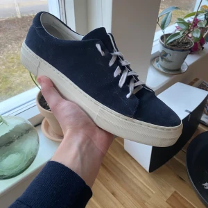 Mörkblå sneakers från These Glory Days - Snygga mörkblå sneakers i mocka från These Glory Days. Skorna har vita snören och en vit sula som ger en stilren look. Perfekta för en avslappnad stil. Storlek 42 riktigt fint skick! 