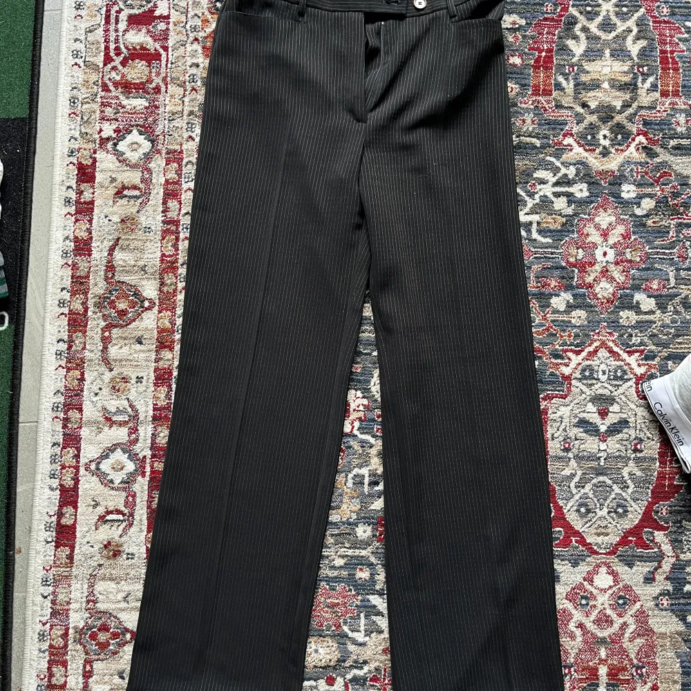 Snygga svarta lågmidjade kostymbyxor från Merrytime med diskreta ränder. I storlek 38 men jag skulle säga att den passar S! Byxorna har en klassisk design med knapp och dragkedja framtill. Tillverkade i 100% polyester för en bekväm passform. Perfekta för en stilren look. . Farkut & Housut.