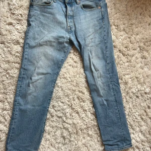Ljusblå jeans från Levi's - Säljer ett par klassiska ljusblå Levi's 501 jeans. De har en rak passform och är tillverkade i slitstarkt denim. Perfekta för en avslappnad stil. Jeansens ikoniska design inkluderar fem fickor och knappgylf. Storleken är 31 32