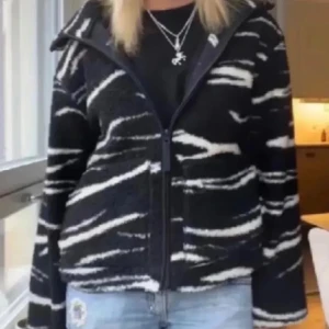 Svart och vit fleecejacka med zebramönster - Säljer en cool svart och vit fleecejacka med zebramönster. Jackan har en dragkedja framtill och hög krage för extra värme. ( lånade bilder) jackan har inga defekter!!!