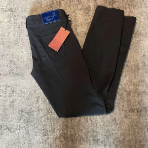 Svarta byxor från Jacob Cohën - Snygga svarta byxor från Jacob Cohën med en klassisk design. Byxorna har en knapp och dragkedja framtill samt fickor både fram och bak. Perfekta för en stilren look.