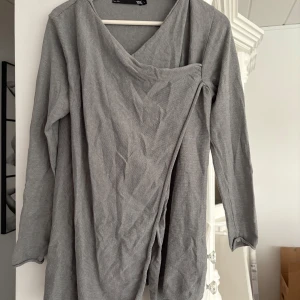 Grå omlottopp från 157 - Säljer en stilren grå omlottopp från 157. Toppen har långa ärmar och en unik omlottdesign framtill. Perfekt för en avslappnad men ändå chic look. Passar bra till både jeans och kjol. 🩶 storlek L 