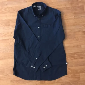 Mörkblå skjorta från Selected Homme - Snygg mörkblå skjorta från Selected Homme i oxfordstil. Tillverkad av ekologisk bomull med en klassisk krage och knappar framtill. Perfekt för vardag och vid finare tillfällen. Skick: 9/10 och använd ett fåtal gånger. Storlek S men passar medium. 