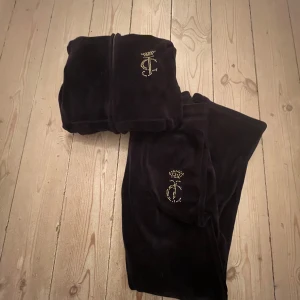 Svart velour hoodie och byxor från Juicy Couture - Säljer en svart velour hoodie och matchande byxor från Juicy Couture. Hoodien har dragkedja och glittrande Juicy Couture-logga på ryggen. Byxorna har en bekväm passform med glittrande detaljer. Perfekt för en avslappnad och stilren look.I storlek 8-9 år men känns och är större, ny pris 1700 och säljer för 900kr skriv för fler bilder