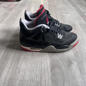 Svarta Nike Air Jordans med röda detaljer - Säljer ett par klassiska svarta Nike Air Jordans med röda och grå detaljer. Skorna har snörning och en ikonisk design med Nike Air-loggan på hälen. Perfekta för sneakerheads som vill ha en tidlös stil.
