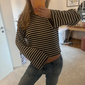 Randig stickad tröja - Säljer en randig stickad tröja i svart och beige. Tröjan har långa ärmar och en croppad passform. Perfekt för en avslappnad stil.