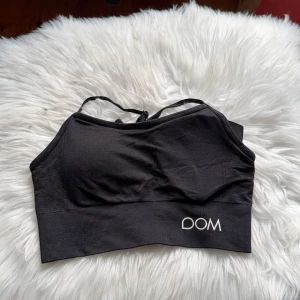 Svart sport-bh från Drop of Mindfulness - Svart sport-bh med smala axelband och logga 'DOM' framtill. Mjuk och stretchig modell som passar perfekt till träning. Materialet är syntet och bh:n har en enkel, stilren design.
