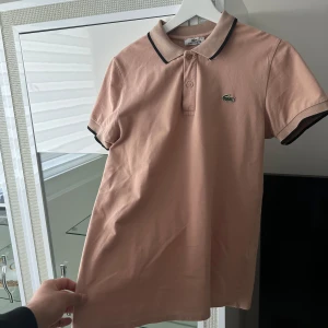Lacoste pike  - Mycket snygg lacoste pike i färgen beige. Säljer pågrund utav att den är liten, mycket bra skick inte använt mycket alls. Storlek: XS/S