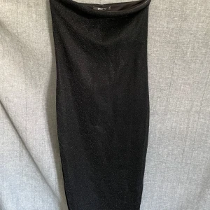 Svart glittrig långklänning  - Säljer en svart långklänning med glittrigt tyg. Klänningen har en enkel, rak passform och är axelbandslös, vilket ger en stilren och elegant look. Perfekt för speciella tillfällen.
