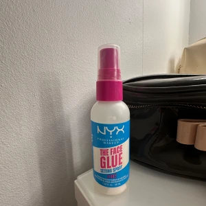 NYX The Face Glue Setting Spray - NYX The Face Glue Setting Spray är en genomskinlig setting spray i en vit och rosa flaska med blå etikett. Perfekt för att fixera sminket hela dagen och ge en fräsch finish. Enkel att applicera med spraymunstycke.