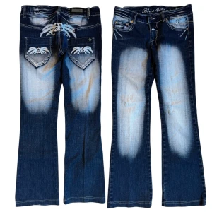 Lågmidjade bootcut blå jeansbyxor med broderade detaljer från Blue Queen - Säljer ett par bootcut lågmidjade blå jeansbyxor från Blue Queen med broderade vita detaljer på bakfickorna och insidan av linningen. Byxorna har en bootcut-stil och ljusa slitningar framtill och baktill för en cool look. Lite för stora för min tjej som brukar ha XS så gissar på storleken som S men skriv för mått ifall det behövs!