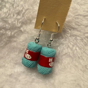 Turkosa garnnystan örhängen - Unika örhängen formade som små turkosa garnnystan med röda band och vita detaljer. Perfekt accessoar för dig som älskar stickning eller vill ha något annorlunda och färgglatt i öronen.krokarna är i sterling silver 