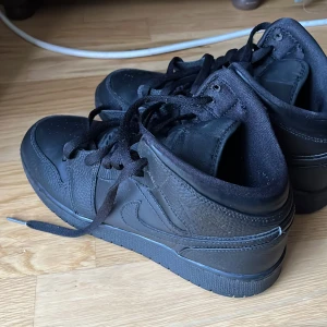 Svarta Nike Air Jordans sneakers - Säljer ett par helsvarta Nike Air Jordans sneakers med klassisk design. Skorna har snörning, rund tå och platt sula. Perfekta för dig som gillar stilrena och sportiga skor. Swoosh-loggan syns på sidan och Air Jordan-detaljer på plösen.