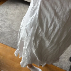 Vit omlottklänning med volang - Säljer en vit omlottklänning med volangdetaljer längs nederkanten. Klänningen har korta ärmar och knyts i midjan för en smickrande passform. Perfekt för sommarens alla tillfällen! Den passar väldigt bra till tex skolavslutningen 💕