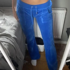 Juicy couture byxor - Säljer ett par blåa mjukisbyxor med bred resår i midjan och dragsko. Byxorna har raka ben, stora fickor fram och bakfickor med knapp. Perfekta för en avslappnad stil.